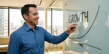 Professional man pointing at growth chart on glass whiteboard in modern office