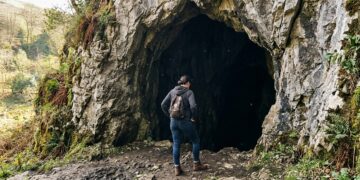 Person standing at the entrance of a dark cave, hesitating before stepping inside