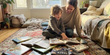A child and parent reading a stack of colorful fun-fact books together on a living room rug
