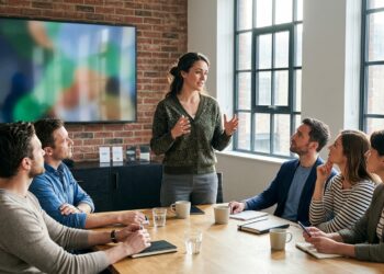 A woman leading a presentation to colleagues in a conference room, speaking directly to the room instead of reading from the screen